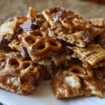 A close-up pile of sweet and salty toffee chex mix recipe pieces coated in caramel, featuring pretzels and chocolate chunks.