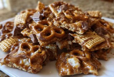 A close-up pile of sweet and salty toffee chex mix recipe pieces coated in caramel, featuring pretzels and chocolate chunks.