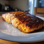 A close-up shot of a beautifully seasoned and crispy air fryer salmon fillet resting on a white plate.