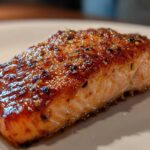 Close-up of a beautifully glazed and cooked piece of air fryer salmon resting on a white plate.