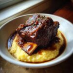 A single, tender braised short ribs piece covered in rich brown glaze resting on creamy yellow polenta.