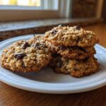 A stack of freshly baked oatmeal cookie with visible chocolate chips resting on a white plate.