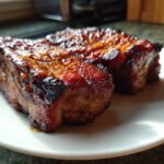 Two pieces of perfectly glazed, caramelized pork steak resting on a white plate.