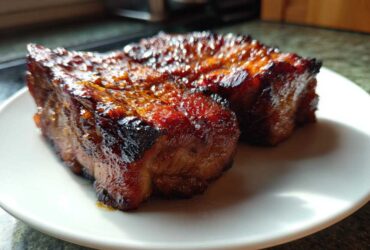 Two pieces of perfectly glazed, caramelized pork steak resting on a white plate.