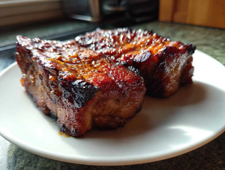 Two pieces of perfectly glazed, caramelized pork steak resting on a white plate.