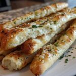 A close-up of several soft, golden breadsticks topped with melted butter, Parmesan cheese, and fresh parsley.