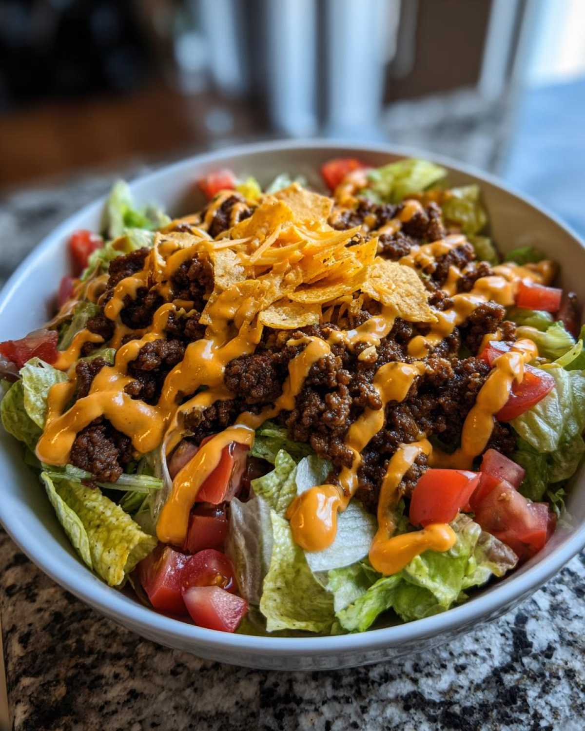 A close-up view of a fresh taco salad featuring lettuce, seasoned ground beef, tomatoes, cheese sauce, and crushed tortilla chips.