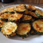 A pile of golden brown, crispy baked parmesan zucchini slices served on a white plate.