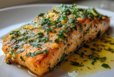 Close-up of a perfectly cooked baked salmon recipe fillet topped with bright green parsley and garlic butter sauce.