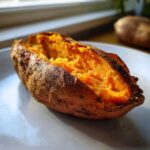 A close-up of a perfectly cooked baked sweet potatoes, split open to reveal the bright orange, fluffy interior.