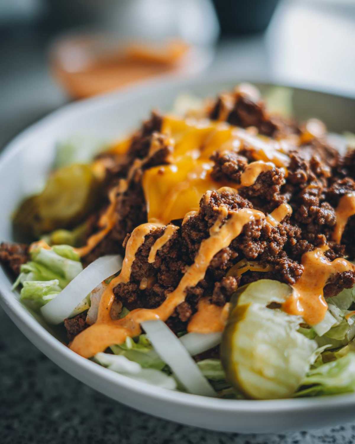 Close-up of a delicious cheeseburger bowl featuring seasoned ground beef, melted cheese, pickles, and special sauce over lettuce.