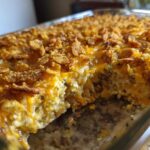 A close-up view of a baked Broccoli casserole in a glass dish, featuring a melted cheese layer and a crunchy, golden cornflake topping.