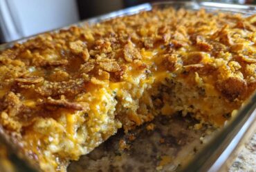 A close-up view of a baked Broccoli casserole in a glass dish, featuring a melted cheese layer and a crunchy, golden cornflake topping.