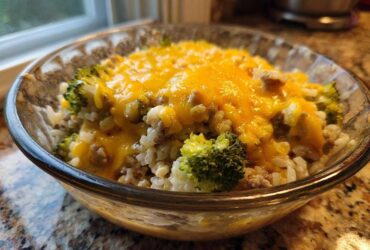 Close-up of a serving of cheesy broccoli rice with ground meat in a clear glass bowl.