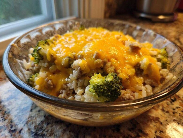 Close-up of a serving of cheesy broccoli rice with ground meat in a clear glass bowl.