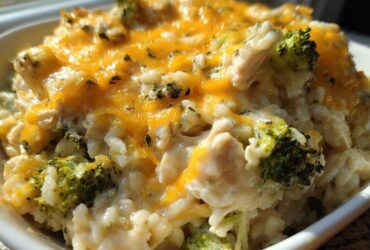 A close-up of a serving of cheesy chicken and rice mixed with bright green broccoli florets, topped with melted cheddar cheese.