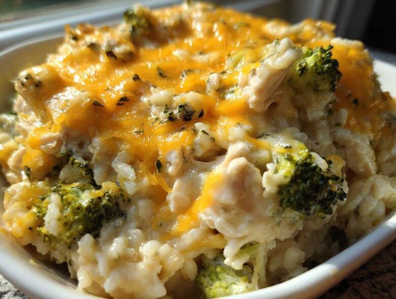 A close-up of a serving of cheesy chicken and rice mixed with bright green broccoli florets, topped with melted cheddar cheese.