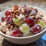 Close-up of creamy chicken salad chick grape salad topped with pecans in a white bowl.