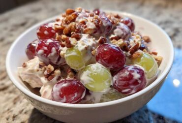 Close-up of creamy chicken salad chick grape salad topped with pecans in a white bowl.