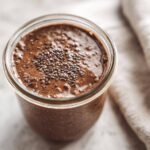 Overhead close-up of rich chocolate overnight oats in a glass jar, topped with a sprinkle of chia seeds.