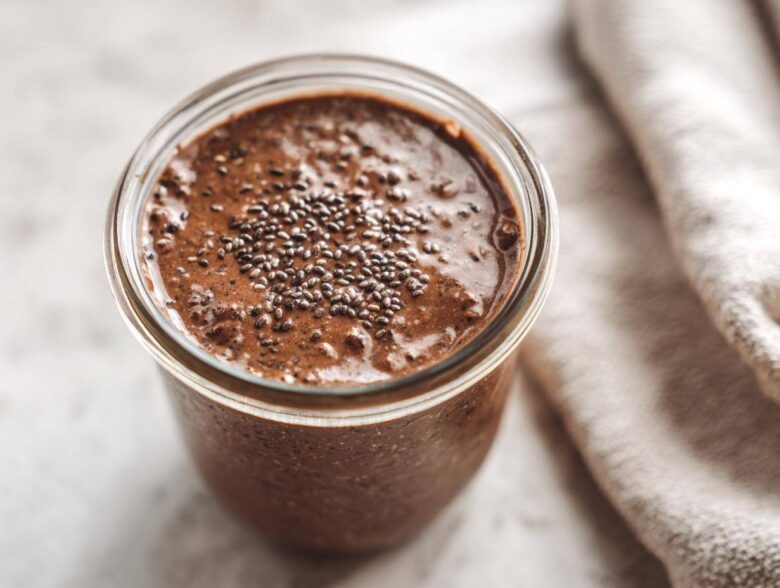 Overhead close-up of rich chocolate overnight oats in a glass jar, topped with a sprinkle of chia seeds.