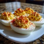 Close-up of five perfectly prepared deviled eggs, piped high with creamy filling and sprinkled heavily with bright red paprika.