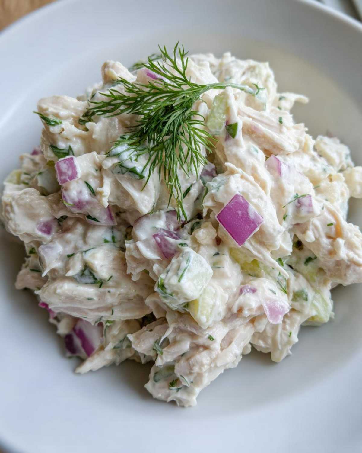Close-up of creamy cottage cheese chicken salad featuring shredded chicken, red onion, cucumber, and topped with fresh dill.