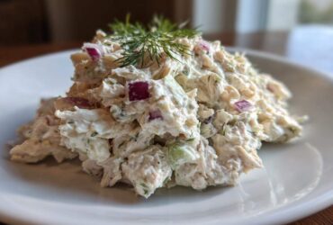 A mound of creamy cottage cheese chicken salad mixed with red onion and topped with fresh dill, served on a white plate.
