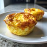 Two freshly baked, golden brown cottage cheese egg cups sitting on a white plate.