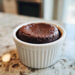A rich, dark chocolate Cottage Cheese Microwave Brownie baked in a white, fluted ramekin on a granite countertop.