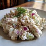 A close-up of creamy cottage cheese chicken salad mixed with red onion and topped with fresh dill.