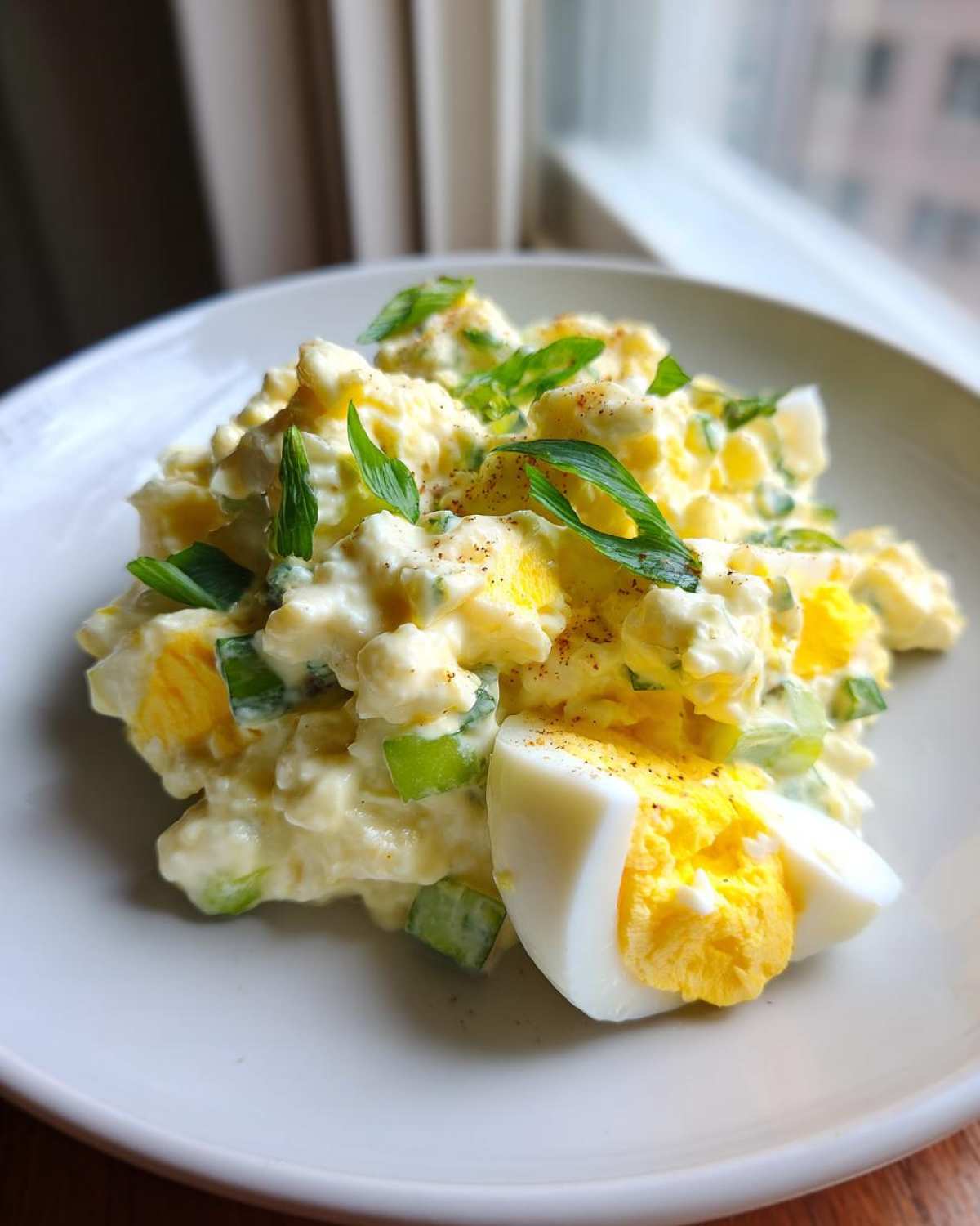 A close-up of creamy egg salad recipe garnished with green onions and a hard-boiled egg wedge.