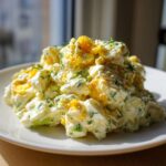 A generous mound of creamy egg salad recipe, featuring visible chunks of egg yolk and white, mixed with herbs, served on a white plate.