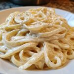 Close-up of fettuccine pasta generously coated in rich, creamy homemade alfredo sauce and black pepper.