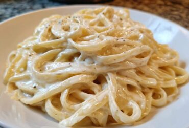 Close-up of fettuccine pasta generously coated in rich, creamy homemade alfredo sauce and black pepper.