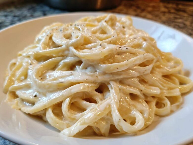 Close-up of fettuccine pasta generously coated in rich, creamy homemade alfredo sauce and black pepper.