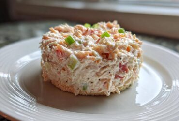 A perfectly molded serving of creamy ham salad with visible celery and red pepper pieces, served on a slice of bread.