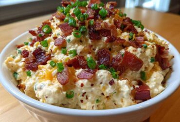 A bowl overflowing with creamy Million Dollar Dip, generously topped with crispy bacon pieces and fresh green onions.