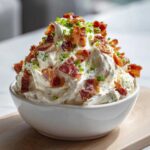 A bowl piled high with creamy Million Dollar Dip, generously topped with crispy bacon bits and fresh green chives.