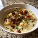 Close-up of a bowl of creamy potato soup recipe garnished generously with crispy bacon bits and fresh chopped chives.