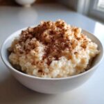 Close-up of creamy rice pudding topped generously with ground cinnamon in a white bowl.