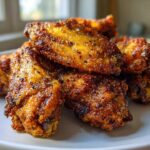 Close-up of perfectly seasoned and crispy air fryer chicken wings piled high on a white plate.