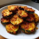 Close-up of golden brown, crispy baked parmesan zucchini slices piled on a white plate.
