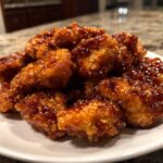 Close-up of crispy, glazed pieces of orange chicken recipe piled high on a white plate.