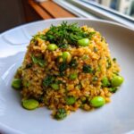 A mound of golden brown crispy rice salad mixed with bright green edamame, topped with fresh herbs.