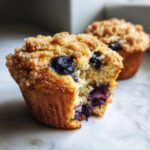 A close-up of a delicious blueberry muffin with a bite taken out, showing the moist interior and crumb topping.