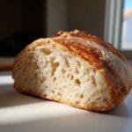 Close-up of a freshly baked Italian bread cut in half, showing a light, airy crumb and a golden, crusty top.