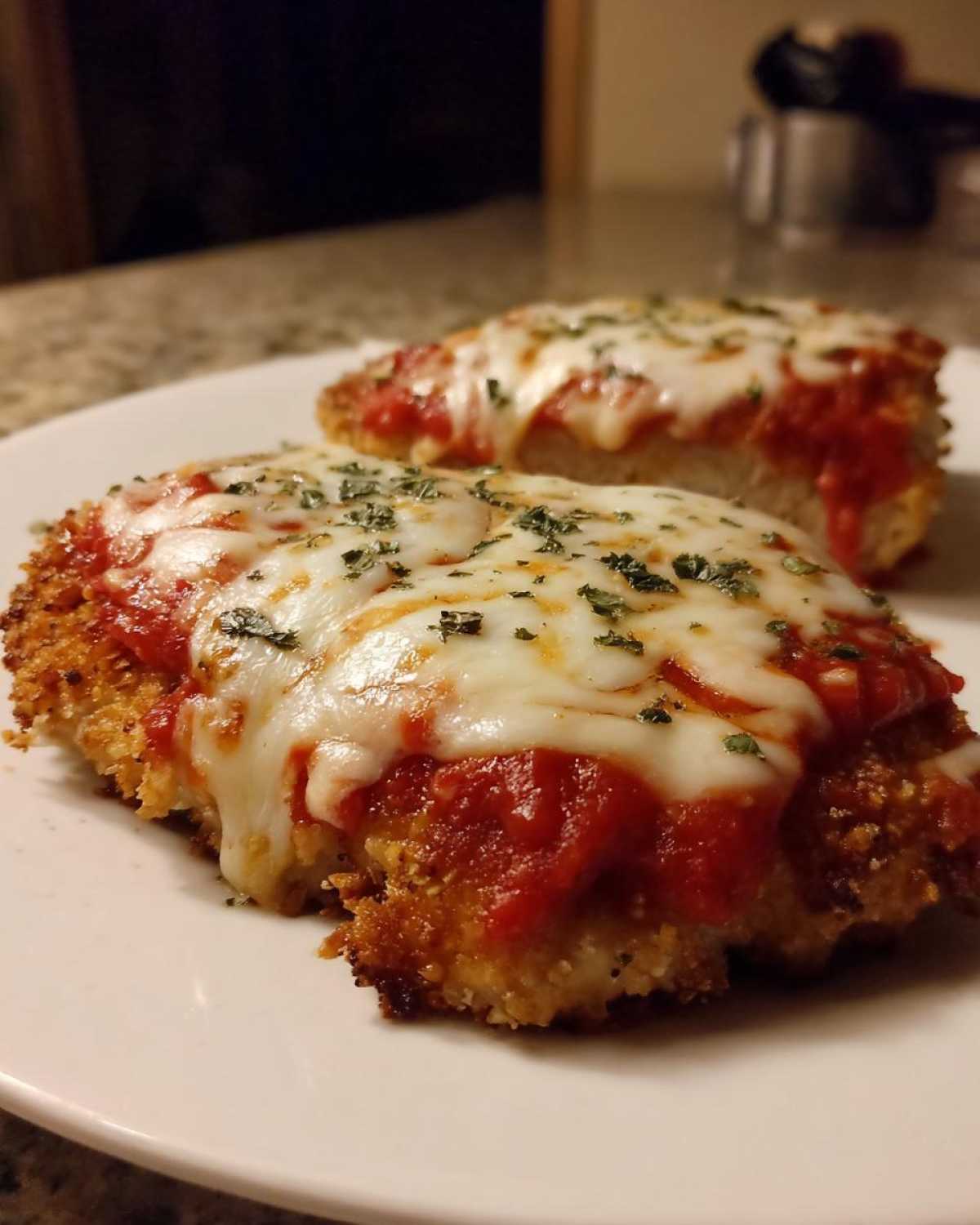 Two servings of Easy Chicken Parmesan featuring crispy breading, marinara sauce, and melted mozzarella cheese, sprinkled with herbs.