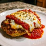 Close-up of a golden-brown breaded cutlet topped with melted mozzarella, marinara sauce, and herbs, representing Easy chicken Parmesan.