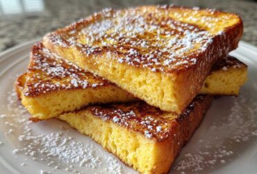Three thick slices of golden brown easy french toast stacked on a white plate and dusted generously with powdered sugar.